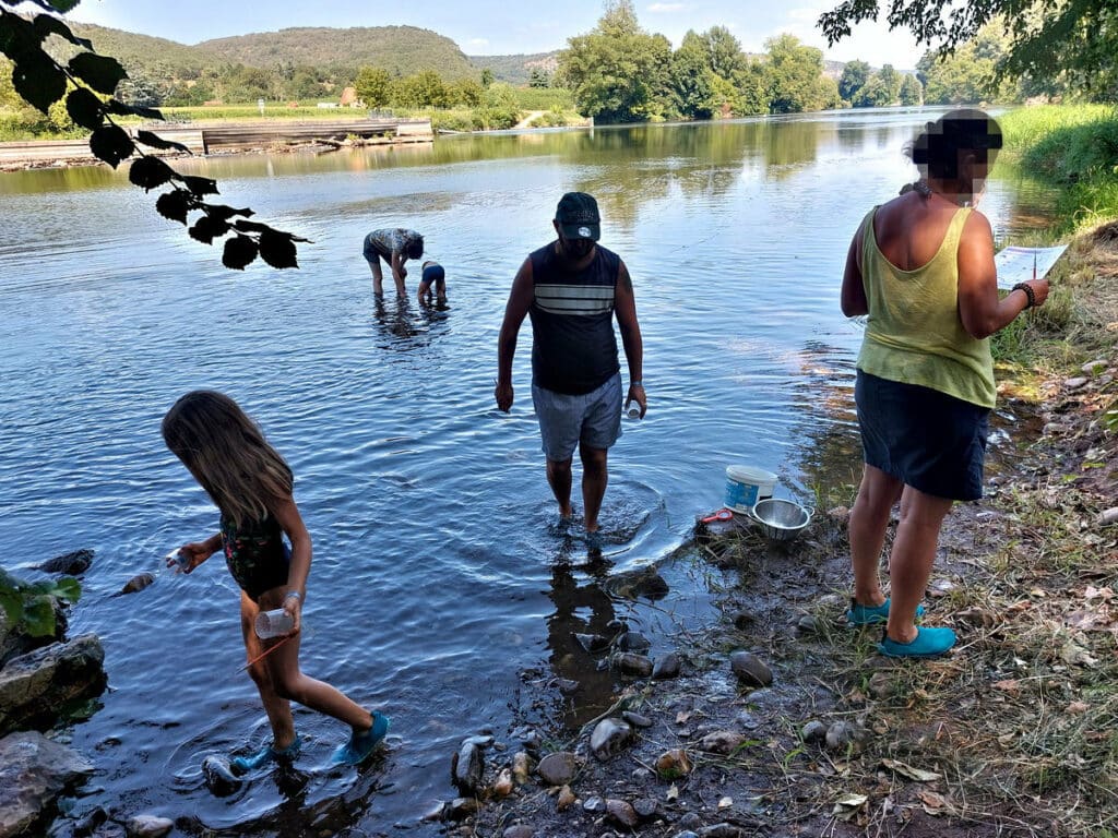 Enfants les pieds dans l’eau explorant la rivière avec épuisettes et boîtes loupe dans le Lot