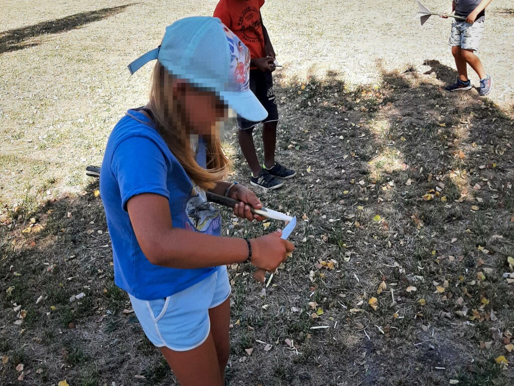 Enfants debout en plein air façonnant des objets avec des outils simples