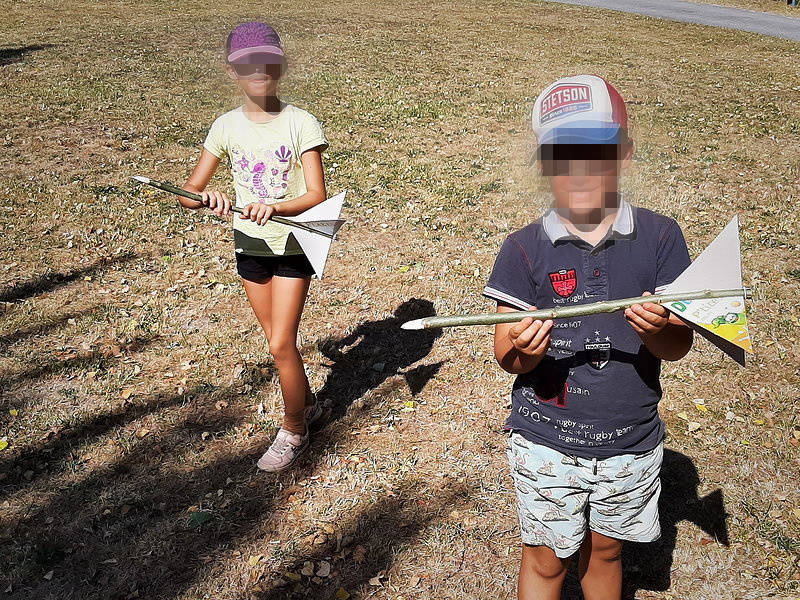 Deux enfants testant des flèches artisanales en bâton et papier en pleine nature