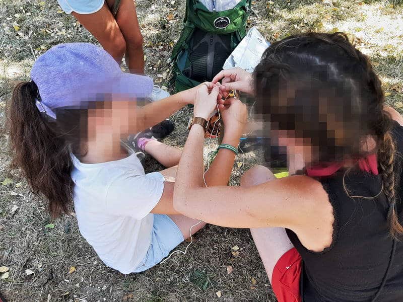 Deux enfants assis dans un sous-bois utilisant des outils simples sous surveillance